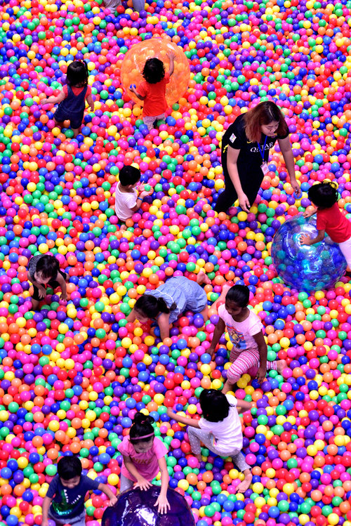 Children of different races enjoying themselves in an enclosure full of colourful balls